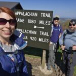 Three smiling hikers in front of an Appalachian trail sign