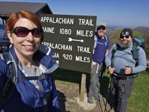Three smiling hikers in front of an Appalachian trail sign